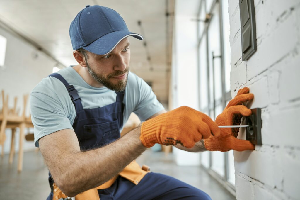 bearded-man-fixing-electrical-wall-socket-with-screwdriver