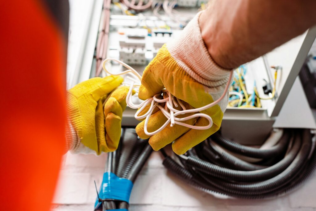 cropped-view-of-electrician-in-gloves-holding-wires-near-electrical-box