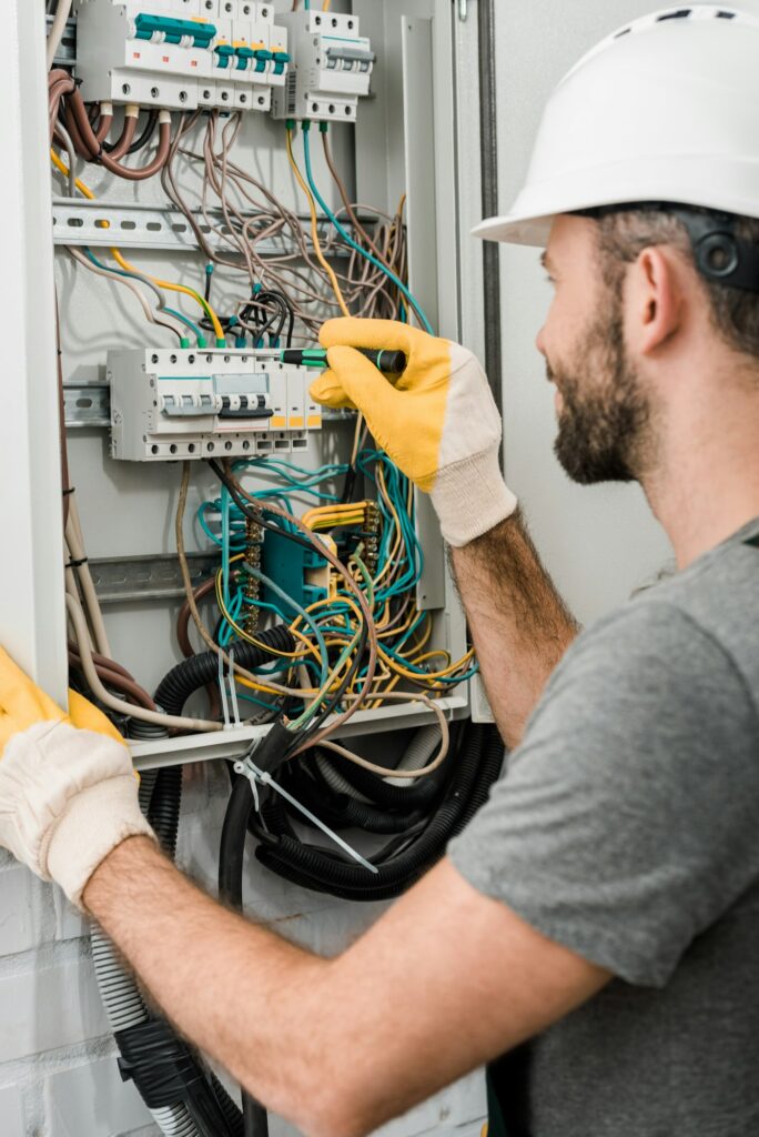 side-view-of-electrician-repairing-electrical-box-and-using-screwdriver-in-corridor